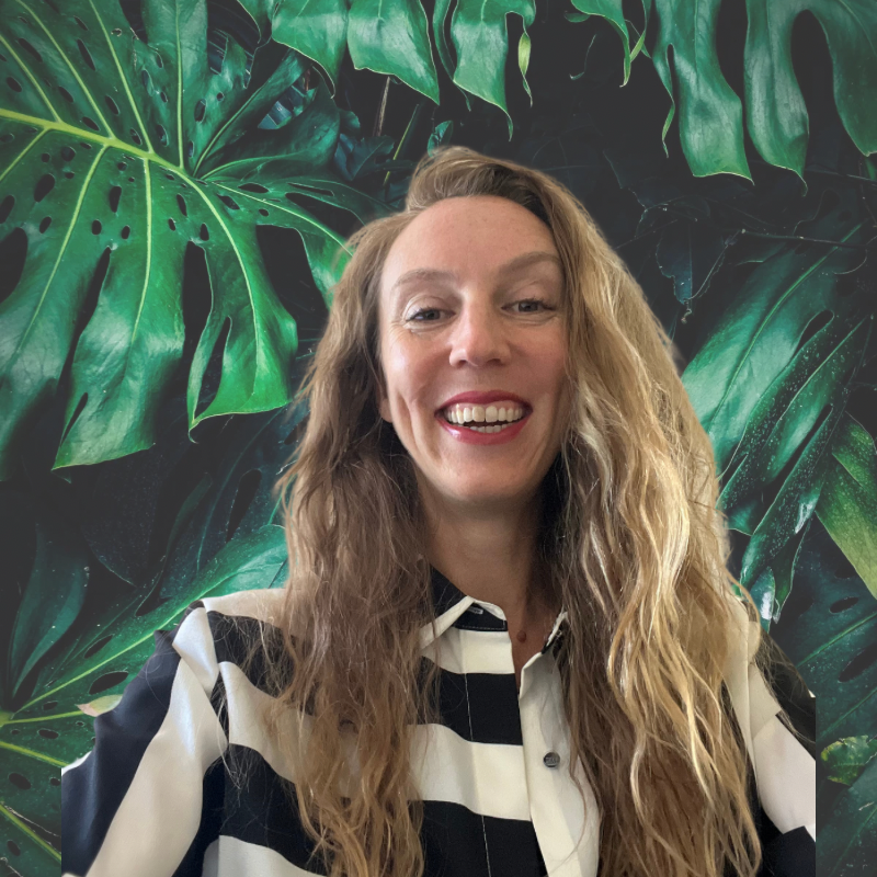 Anita, founder of MagnaGem Marketing Group, smiling in front of monstera leaves